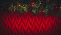 A Chrismas tree branch with glowing garland on red knitted background