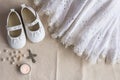 Christening background with baptism dress, shoes, candles and crystal cross pendant on white linen cloth - top view
