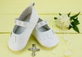 Christening background of white booties and pendant cross on yellow painted wood table