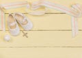 Christening background with white shoes, candle and crystal cross pendant on yellow painted wooden background