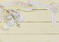 Christening background with white shoes, candle and crystal cross pendant on yellow painted wooden background