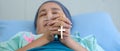 Christian cross in hands of cancer patient wearing headscarf during chemotherapy treatment lying on bed in hospital praying and Royalty Free Stock Photo