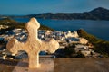 Christian cross and Plaka village on Milos island over red geranium flowers on sunset in Greece Royalty Free Stock Photo