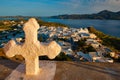 Christian cross and Plaka village on Milos island over red geranium flowers on sunset in Greece Royalty Free Stock Photo