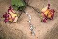 Christian cross on rosary and a dry yellow red roses lie on a sandstone Royalty Free Stock Photo