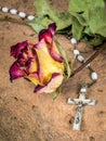 Christian cross on rosary and a dry yellow red roses lie on a sandstone Royalty Free Stock Photo