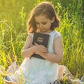 Christian girl holds bible in her hands. Reading the Holy Bible in a field during beautiful sunset. Concept for faith Royalty Free Stock Photo