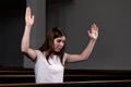 A Christian girl in white shirt is sits with his hands up and face and praying with humble heart in the church