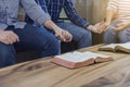 A christian group holding hands and together over blurred bible on wooden table, fellowship or bible study concept