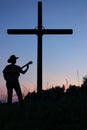 Christian religion view - silhouette of young man with hat play the guitar and sing praise the God below shape of cross with