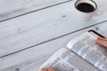 Christian woman holding and reading from open holy bible book placed on wooden table with a cup of coffee Royalty Free Stock Photo