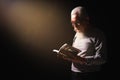 Senior man standing in dark background holding and reading holy bible Royalty Free Stock Photo