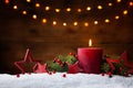 Christmas or advent candle, fir branches, berry and red stars in snow against light  garland background. Holiday card Royalty Free Stock Photo