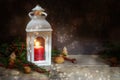 Christmas and Advent decoration, red candle with warm light in a white lantern, fir branches and nuts on rustic wooden planks Royalty Free Stock Photo