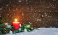 Christmas or Advent wood background with burning red candle on snow and snowflakes, decorated with fir branches and ornaments. Royalty Free Stock Photo