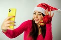 Christmas advertising Young girl taking selfie with phone She is wearing a Christmas hat Christmas tree toys She has Royalty Free Stock Photo