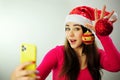 Christmas advertising Young girl taking selfie with phone She is wearing a Christmas hat Christmas tree toys She has Royalty Free Stock Photo