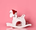 Christmas antique rocking white horse toddler toy in new year red hat on pink Royalty Free Stock Photo