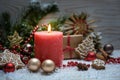 Christmas arrangement with a red burning candle, fir branches, baubles and ornaments in the snow against a wooden background Royalty Free Stock Photo