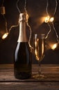 Christmas background with a bottle of champagne and a full glass on the background of a glowing garland in the dark. Royalty Free Stock Photo