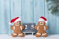 Christmas background with gingerbread men cookies in Santa hats and block calendar with 25 December, wooden background with fir Royalty Free Stock Photo