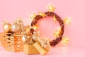 Christmas background in gold glitter color - Christmas wreath, balls, gift box and glowing stars lights on light pink background. Royalty Free Stock Photo