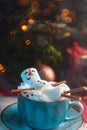 Christmas background with a marshmallow man lying in a mug with cocoa, in the background a Christmas tree with toys, a garland and Royalty Free Stock Photo