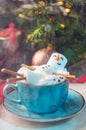 Christmas background with a marshmallow man lying in a mug with cocoa, in the background a Christmas tree with toys, a garland and Royalty Free Stock Photo
