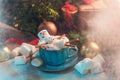 Christmas background with a marshmallow man lying in a mug with cocoa, in the background a Christmas tree with toys, a garland and Royalty Free Stock Photo