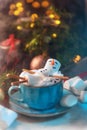 Christmas background with a marshmallow man lying in a mug with cocoa, in the background a Christmas tree with toys, a garland and Royalty Free Stock Photo