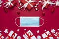 Christmas background during pandemic of Covid 19 made from face mask, gift boxes and decorations on red background Royalty Free Stock Photo