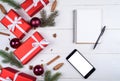 Christmas background with red gift boxes, mobile phone with white screen and blank notebook, copy space. Template for new year. Royalty Free Stock Photo