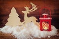 Christmas background with red lantern, wooden decorative reindeer and tree on the snow over wooden background.