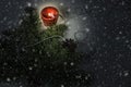 Christmas background with spruce branch, cone, lighted red candle and small beads. Falling snow in foreground.