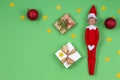 Christmas background. Toy elf, present boxs, red baubles, confetti glitter stars on light green background Royalty Free Stock Photo