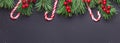 Christmas background with tree branches, candy cane and holly on black wooden background. Snowfall drawing effect Royalty Free Stock Photo