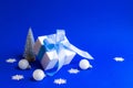 Christmas background. White gift box with blue ribbon, winter tree, Snowflakes and Silver balls in xmas composition on blue Royalty Free Stock Photo
