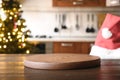 Christmas background with wooden table top, Santa hat, and blurred holiday decorating kitchen