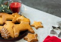 Christmas baked cookies of various shapes, a sprig of a coniferous tree and a red candle are on a dark gray background.