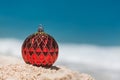 Christmas Ball colored Red on the Sandy Beach, Holiday and Vacation Concept