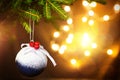 Christmas ball with snow, red berries and a bow on a live branch of a fir tree with Golden lights of garlands in defocus. New year Royalty Free Stock Photo