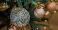 Christmas ball with turquoise glass stones and golden shiny blurry balls on a green branch with a yellow garland. Bokeh Royalty Free Stock Photo