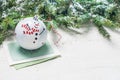 Christmas bauble decorated with joyful snowman on Christmas card next to fir tree branches on white textured background Royalty Free Stock Photo