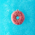 Christmas bauble decoration made of pink doughnut with snow on blue background. Minimal New Year concept Royalty Free Stock Photo