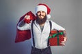 bearded smiling man in Santa's hat in white shirt holds sack and gift box. New Year concept Royalty Free Stock Photo