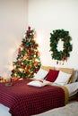 Christmas bedroom interior in white and red colors. Double bed with plaid blanket and Christmas tree Royalty Free Stock Photo