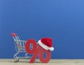 Christmas big sales: shopping cart with Santa hat and symbol of percent on wooden background over dark blue wall Royalty Free Stock Photo