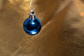 Christmas blue ball hanging on a golden glittering background. Template for postcards, congratulations, copy space