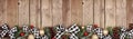 Christmas border banner with white and black checked buffalo plaid ribbon, ornaments and branches, above view on a wood background