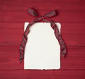 Christmas Bow that is Red and Green plaid with Vintage Paper with ragged edges on Rustic Wood Boards Background with copy space Royalty Free Stock Photo